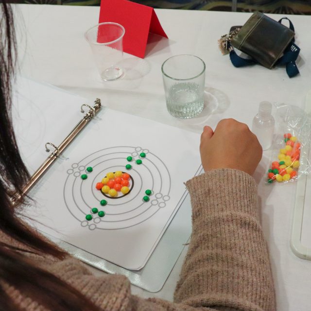 A woman at a table using candy to create a diagram of neutrons and electrons.