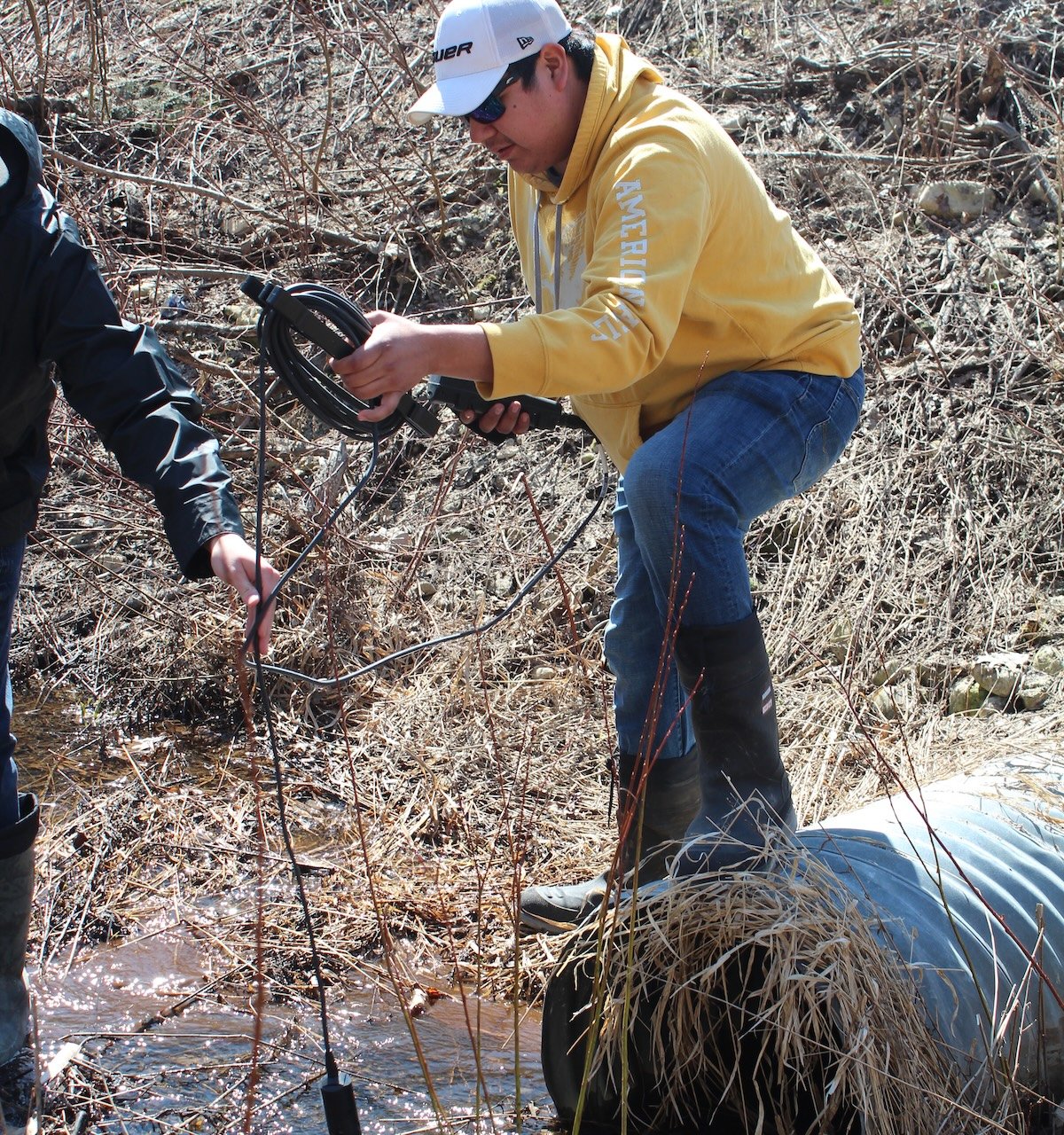 Man in yellow jacket taking water quality measurements in a stream.