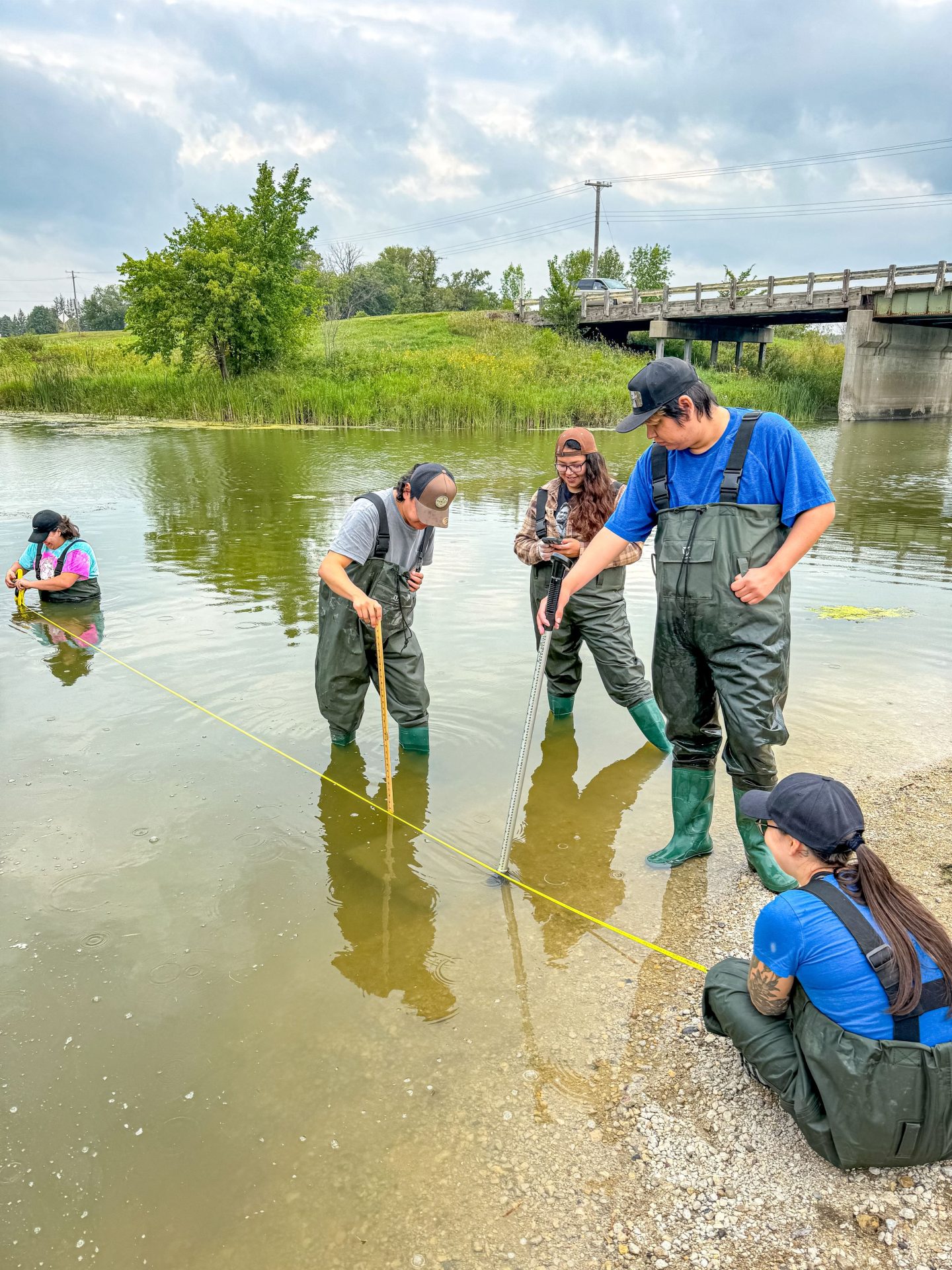 Young adults wearing waders are standing in a lake.